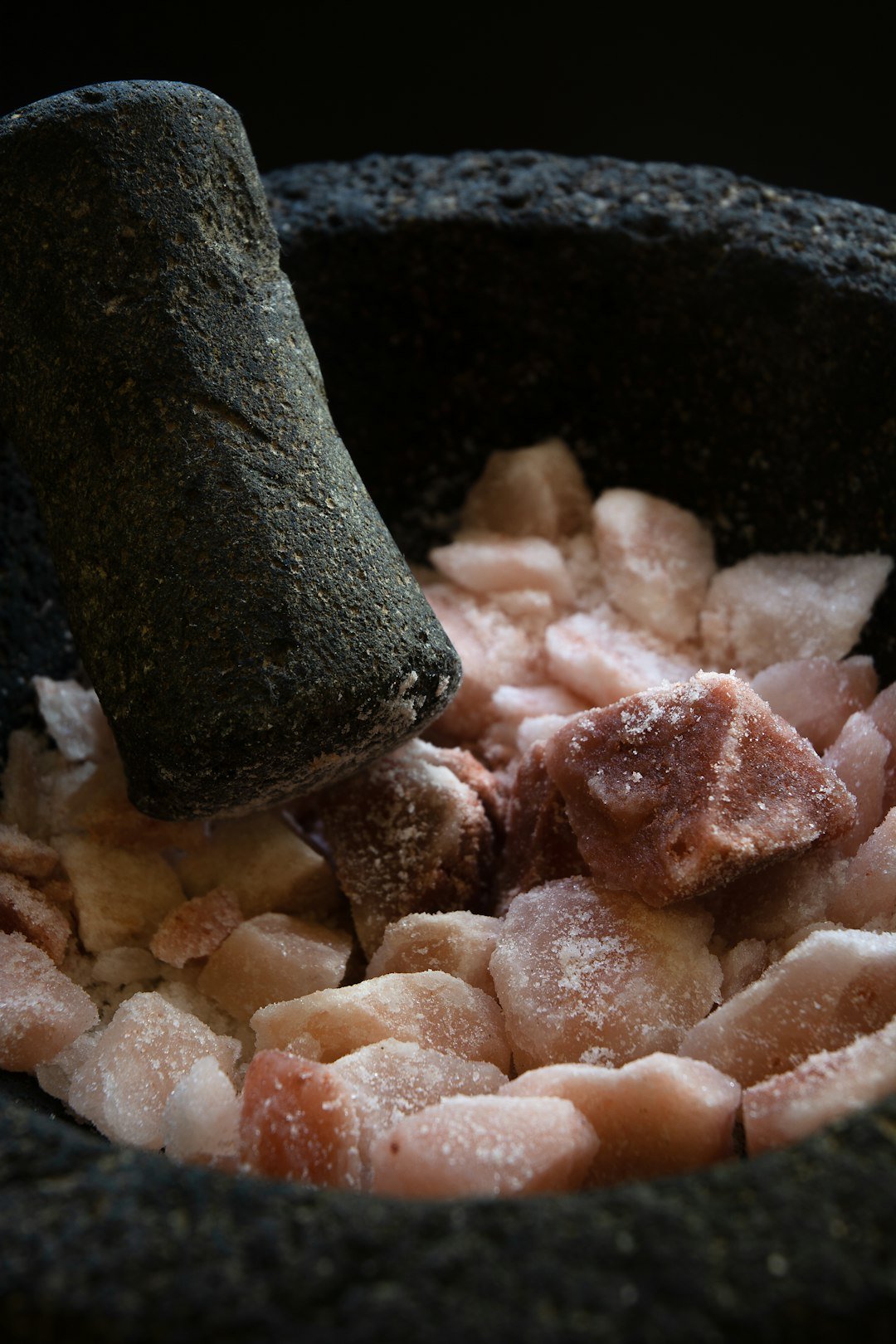 Grinding lumps of pink himalayan salt in a traditional mexican mortar.