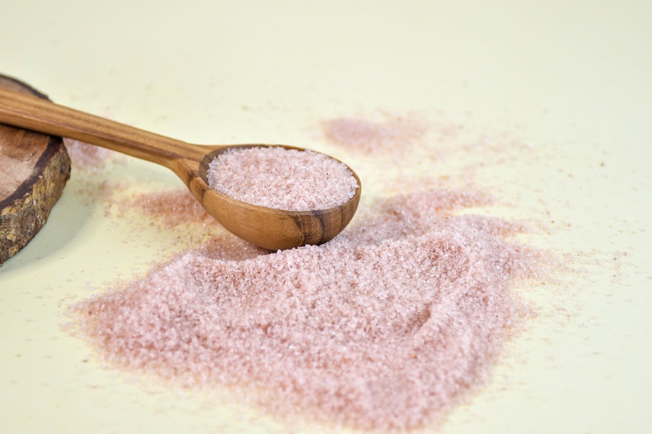 Pink Himalayan salt scattered with a wooden spoon on a light background.